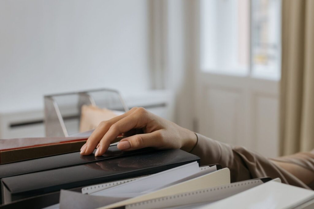 Hand resting on a stack of file folders by a window